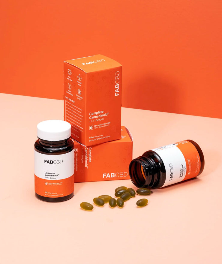 Three FAB CBD supplement bottles and boxes on a peach-orange background with green softgel capsules spilled from one bottle.