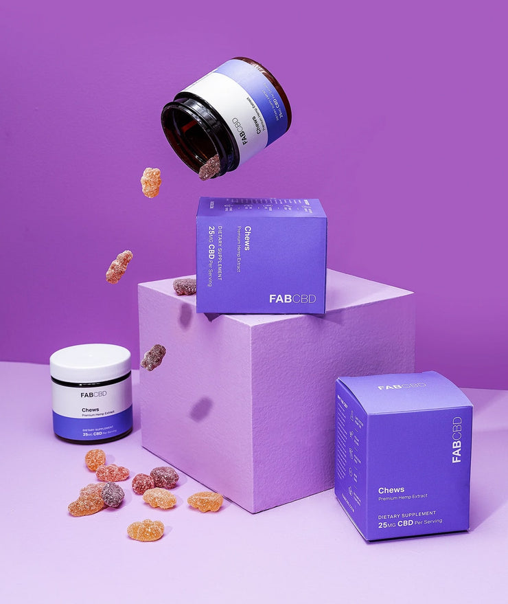FABCBD purple-chew gummies jar and two purple product boxes arranged on a lavender pedestal with gummies falling around them