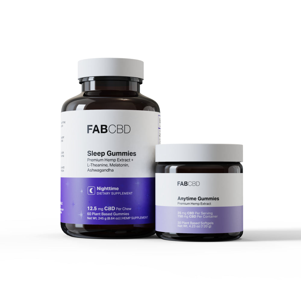Two dark amber glass jars with white lids standing side-by-side against a pure white background. The larger jar on the left is for FAB CBD "Sleep Gummies" featuring a formula of "Premium Hemp Extract + L-Theanine, Melatonin, Ashwagandha" and a dark purple "Nighttime DIETARY SUPPLEMENT" banner displaying specifications: "12.5 mg CBD Per Chew," "60 Plant Based Gummies," and "Net Wt. 245 g (8.64 oz)." The smaller jar on the right is for FAB CBD "Anytime Gummies" featuring "Premium Hemp Extract" and a light pur